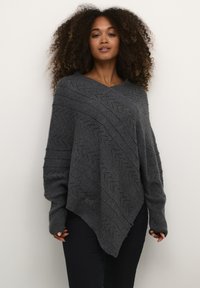 Poncho grigio lavorato a maglia con scollo a V, caratterizzato da un motivo a zigzag e maniche ampie. L'orlo è asimmetrico, enfatizzando la texture e il design.