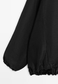 Schwarzer Langarmshirt mit Puffärmeln sowie elastischen Bündchen und Saum, strukturierter Stoff, freigestellt vor weißem Hintergrund.