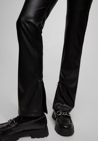 Pantalon évasé en similicuir noir avec fermetures éclair latérales ; texture lisse, taille haute et coupe ajustée. Assorti à des mocassins noirs épais.