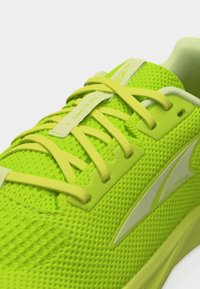 Pohled zblízka na běžeckou botu jasně žluto-zelené barvy s prodyšným svrškem z mesh materiálu, křížovými tkaničkami a logem na boční straně.