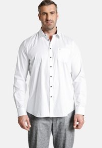 Weißes Button-Down-Hemd aus Baumwolle mit langen Ärmeln, schwarzen Knöpfen und einer einzelnen Brusttasche, die ein kleines Logo-Detail aufweist.