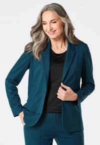 Teal blazer in glad stof met een enkele knoop en notch revers, gecombineerd met een zwart top, met een getailleerd ontwerp en lange mouwen.