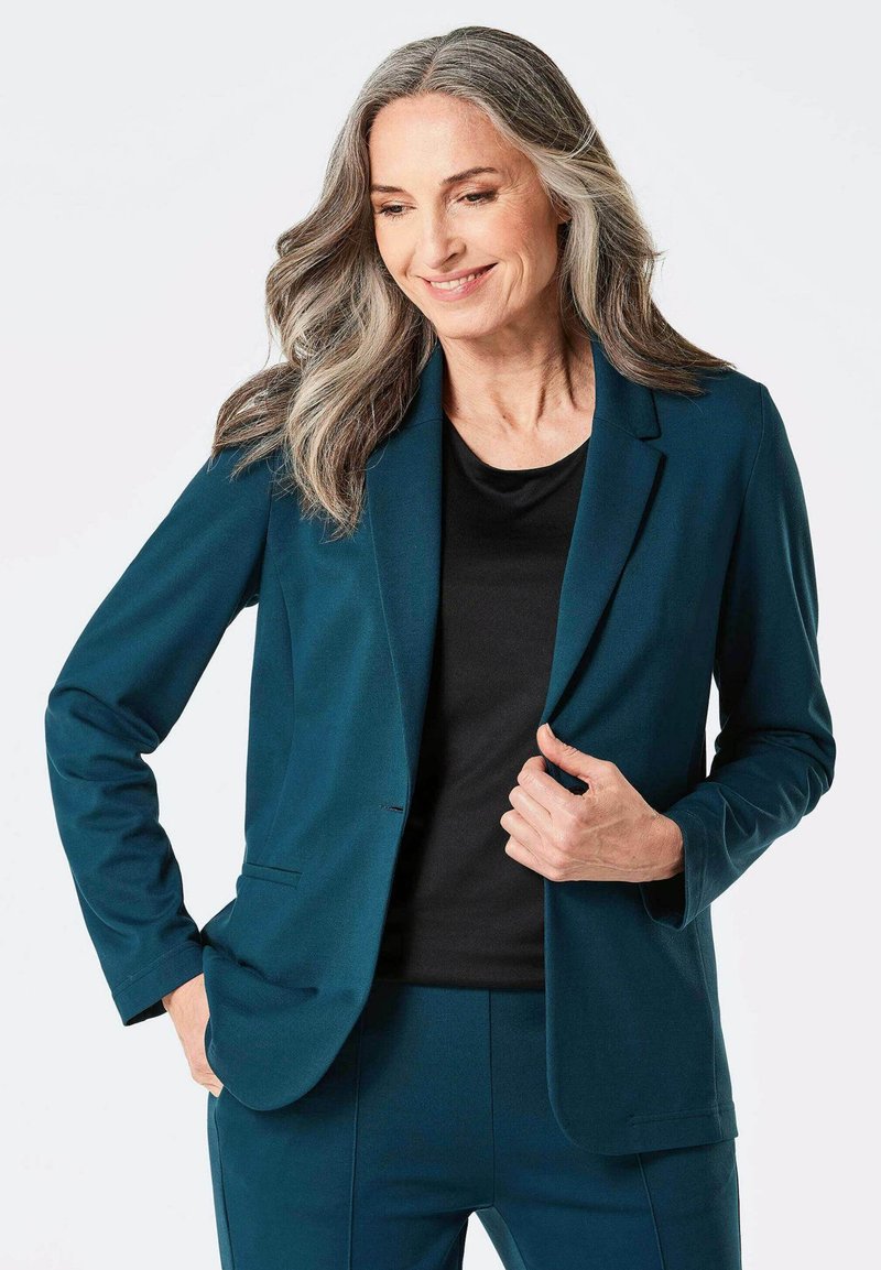 Teal blazer in glad stof met een enkele knoop en notch revers, gecombineerd met een zwart top, met een getailleerd ontwerp en lange mouwen.