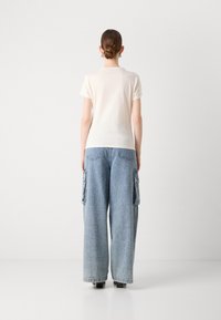 Cream short-sleeve t-shirt paired with blue wide-leg cargo jeans featuring side pockets and a relaxed fit. Smooth texture and casual style.