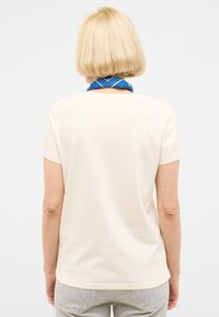 Camiseta de manga corta crema con escote redondo, textura suave y corte recto, combinada con una bufanda de cuello azul con patrón.