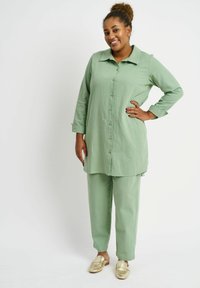 Light green, button-up tunic with long sleeves, paired with matching pants and gold slip-on shoes. Fabric appears soft with a subtle texture.