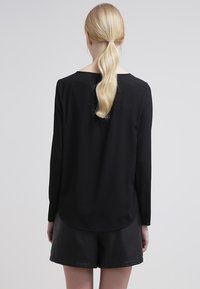 Zwarte top met lange mouwen, ronde halslijn en een ronde zoom, gemaakt van lichtgewicht stof. Gemaakt in combinatie met zwarte leren shorts met een gestructureerde afwerking.