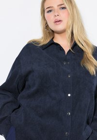 Camicia in corduroy blu navy con colletto, due tasche frontali e bottoni a scatto argento. Tessuto morbido con maniche lunghe.