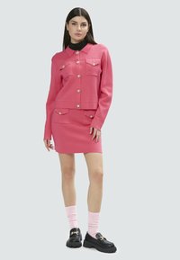 Conjunto de chaqueta y falda de punto rosa con cuatro bolsillos, detalles de botones, usado con calcetines rosas y mocasines negros gruesos. Textura suave.