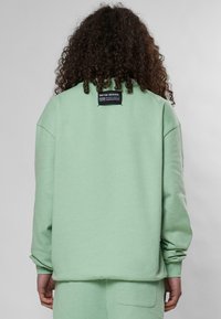 Felpa verde menta con una vestibilità morbida, polsini a coste e una piccola etichetta nera sul retro. Tessuto morbido con una texture liscia.