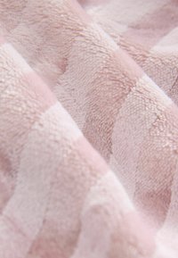 Pehmeä vaaleanpunainen viltti, jossa on pöyheä rakenne ja ruutukuvio eri sävyissä vaaleanpunasta ja valkoisesta, mikä lisää visuaalista syvyyttä.