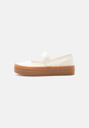 Fehér vászon Mary Jane cipő vastag barna gumitalppal és egy pánttal a tetején.