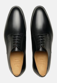 Chaussures habillées en cuir noir avec une finition lisse, dotées d'un laçage et d'un bout arrondi. L'intérieur comprend des détails de marque.