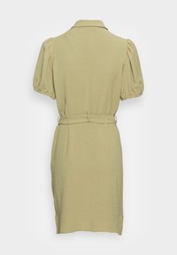 Vestido verde pálido, com colarinho, mangas curtas bufantes e cintura com cinto. Apresenta um tecido texturizado e um corte até ao joelho.
