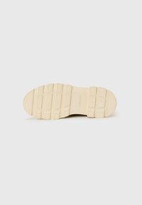 Semelle de basket en caoutchouc beige avec une surface texturée, présentant des motifs rectangulaires et circulaires pour une meilleure adhérence et traction.