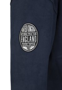 Marine sweatshirtstof met een ronde zwart-witte geborduurde patch met de tekst "Verenigd Koninkrijk Nationaal Polo Team Engeland Speler Captain 1987."