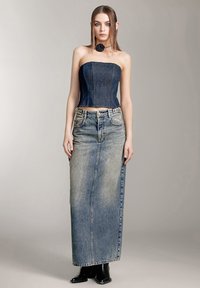 Top strapless de mezclilla cortado con un diseño ajustado, combinado con una falda larga de mezclilla de talle alto en un lavado azul desgastado. Botines negros.