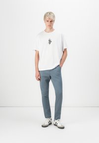 Hvit t-skjorte med rund hals og svart grafikk, sammen med lys blå smale bukser og hvite sneakers med svarte striper og grå detaljer.