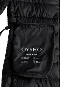 Fekete, csomagolható tasak "OYSHO PACK & GO" felirattal és ikonokkal, amelyek a 100% toll, légáteresztő, vízlepergető és szélálló jellemzőket jelzik.