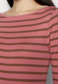 Långärmad topp med en bred halsringning, som har växelvis rosa och bruna horisontella ränder på en texturerad väv.