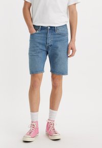 Denim shorts in light blue with a straight fit, featuring a classic five-pocket design and subtle whiskering, paired with pink high-top sneakers.