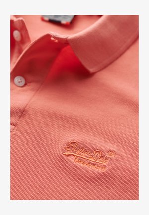 Polo shirt corallo con tessuto testurizzato, caratterizzato da un logo ricamato a contrasto sul lato sinistro del petto e bottoni bianchi sulla patta del colletto.
