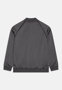 Grå idrottsjacka med ribbat krage och muddar, tillverkad av ett mjukt, lätt tyg. Enkel design, inga synliga logotyper eller mönster.