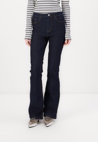 Mörkblå utsvängda jeans med hög midja, med framfickor, knäppning och sömnad detaljer längs sömmarna.