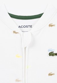 Λευκό βαμβακερό φούτερ με πράσινο γιακά, κεντημένα λογότυπα κροκοδείλων σε χρυσό, κίτρινο, μπεζ και πράσινο, με μπροστινό κούμπωμα.