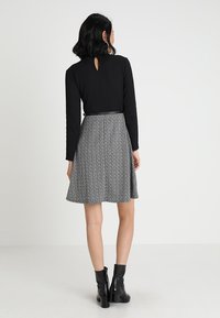 Svart långärmad topp med nyckelhål baktill, kombinerad med en grå mönstrad kjol med utsvängda nederkant. Bärs med svarta ankelboots.