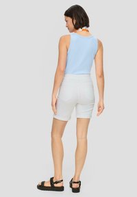 Jasnoniebieski top bez rękawów, białe szorty dżinsowe z podwiniętymi nogawkami i czarne sandały. Prosty fason, gładka faktura i luźny krój.