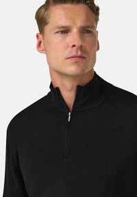 Melna puszipaļa pulovers ar augstu apkakli. Ribota tekstūra un gludais rāvējslēdzējs. Tuva piegriezuma dizains, minimālisma stils.