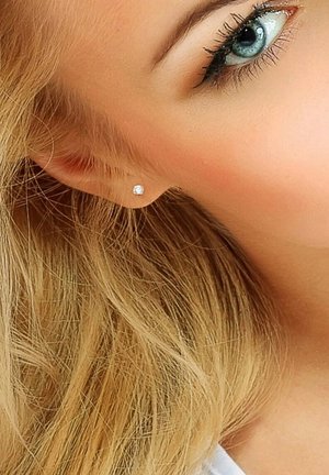 Boucles d'oreilles en argent ornées d'une pierre précieuse transparente, mises en valeur par des cheveux blond clair et une peau pâle, avec des accents de maquillage subtils.