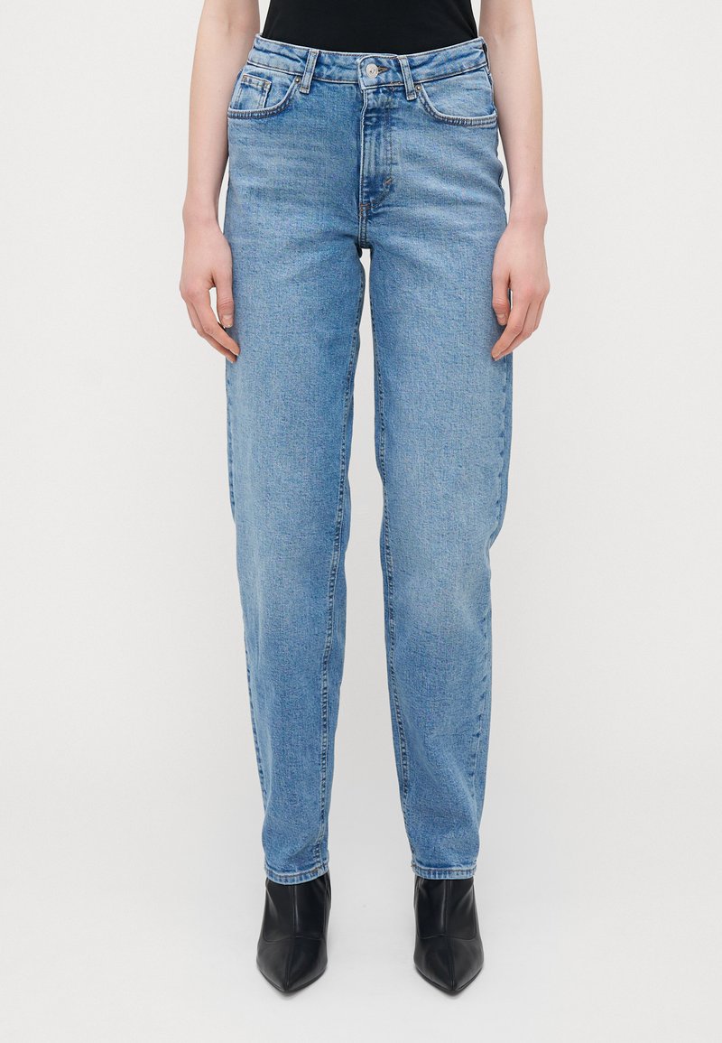 Ανοιχτό μπλε ψηλοκάβαλο τζιν με ίσια γραμμή, διαθέτει φερμουάρ, σχεδίαση με πέντε τσέπες και ελάχιστη φθορά, συνδυασμένο με μαύρες γόβες.