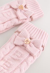 Lyserøde strikkede vanter med ribbet kant, prydet med en stor sløjfe og guldfarvet hjerteformet hardware med blomsterformet udskæring.