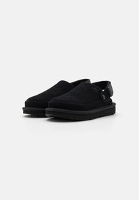 Sorte semskede slip-on sko med avrundet tå, elastisk bakre stropp og strukturert gummisåle. Minimalistisk design uten synlige mønstre.