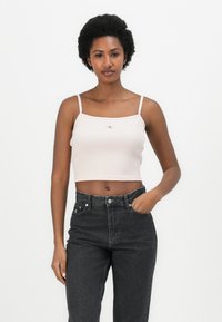 Light pink ribbed crop top with thin straps, featuring a small logo on the chest. Paired with high-waisted dark denim jeans.