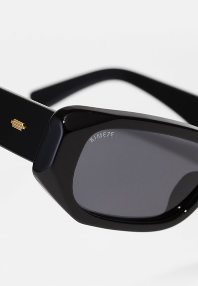 Ochelari de soare negri cu o ramă geometrică, lentile întunecate și branding subtil. Au un accent auriu pe lateral și o textură netedă.