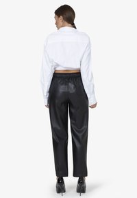 Witte, cropped shirt met een relaxed fit, gecombineerd met hoge zwart faux leren broek. Gladde textuur, minimalistisch ontwerp en elastische tailleband.