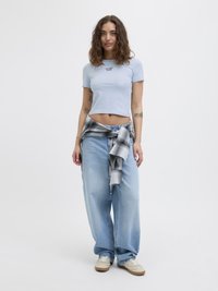 Lyseblå kort t-skjorte med tekst, kombinert med løse lyseblå jeans, knyttet grå rutete skjorte rundt livet, og beige joggesko.