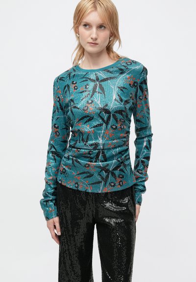 Haut à manches longues en teal avec un motif floral noir et orange, fabriqué en tissu texturé. Assorti à un pantalon pailleté noir brillant.