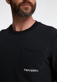 Felpa nera a collo rotondo realizzata in cotone, con tasca frontale e testo "TUFFSKULL" in bianco. Collo a costine e texture liscia.