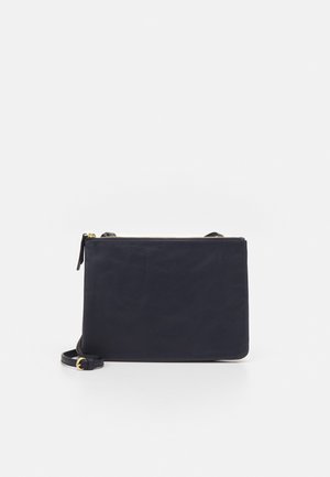 Sac bandoulière en cuir noir avec fermeture éclair dorée et sangle réglable placé sur un fond blanc.
