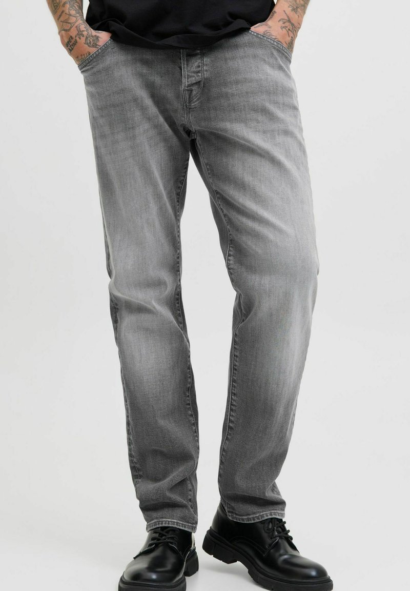 Jeans en denim gris avec une coupe décontractée, dotés de poches avant et d'un léger délavage, associés à des chaussures en cuir noires.