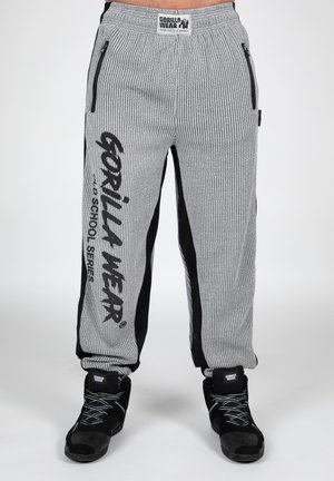 Grijze geribde joggpants met zwarte zijpanelen; beschikt over ritszakken en opvallende branding in vetgedrukte letters op het linkerbeen.