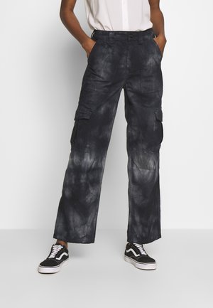 Mørkeblå cargos med en falmet, tie-dye tekstur. Funktioner inkluderer flere lommer og en afslappet, bred benpasform. Parret med sorte sneakers.