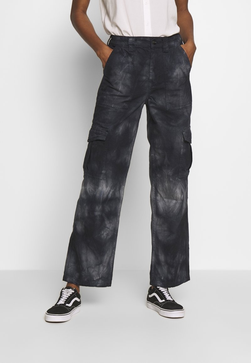 Pantalones cargo de color azul oscuro con una textura desteñida de tie-dye. Incluye múltiples bolsillos y un ajuste relajado de pierna ancha. Combinados con zapatillas negras.