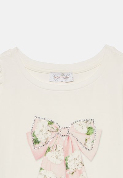 Άσπρο βαμβακερό μπλουζάκι με φιογκάκι σε λουλουδάτο μοτίβο σε ροζ, περιγράμμα με διάφανα στρας. Η ετικέτα γράφει "MONNALISA."