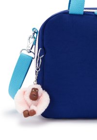 Bolsa de tela azul marino con un diseño voluminoso, que cuenta con una correa azul cielo y un charm de mono esponjoso rosa con cara marrón y pequeños ojos blancos.