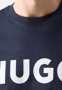 Navyblaues Baumwoll-T-Shirt mit einem auffälligen weißen "HUGO"-Logo in fetter Typografie. Einfacher runder Ausschnitt und glatte Textur.